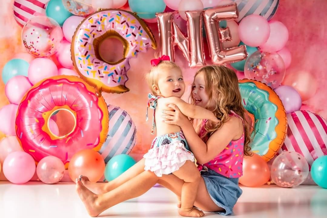 Happy sisters sitting in front of donut birthday backdrop