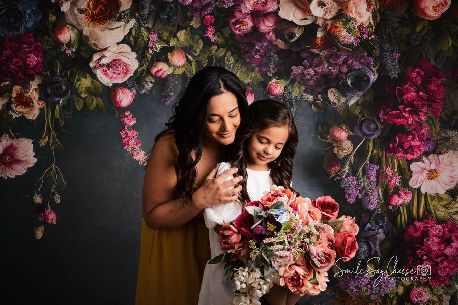 Mother holding her daughter in front of floral backdrop