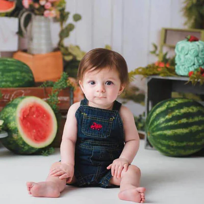 Boy in overalls sitting in front of summer watermelon backdrop