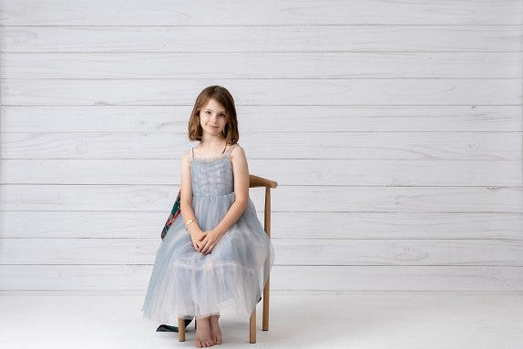 Girl in grey skirt sitting in front of white wood grain vinyl backdrop