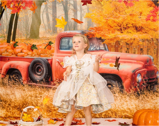Girl playing with maple leaves in front of autumn orange truck backdrop