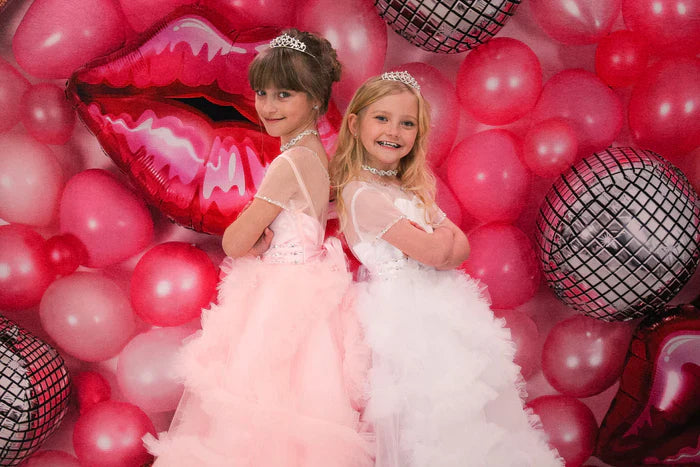 Two sisters standing back to back in front of a Barbie pink backdrop
