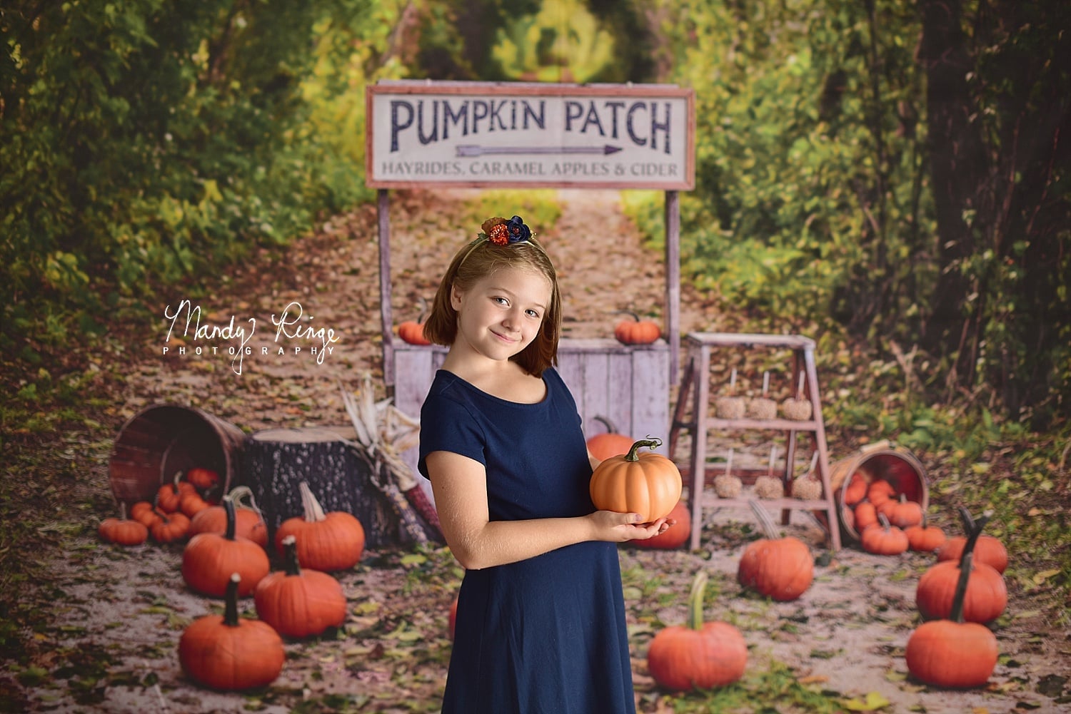 Girl holding a pumpkin standing in front of a pumpkin stand