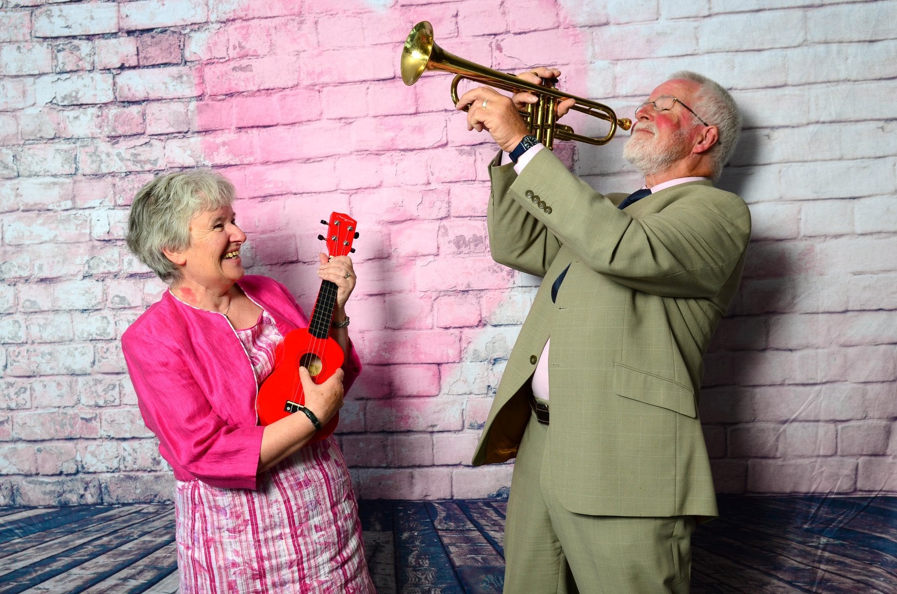 Elderly couple performing musical instruments standing in front of Valentine's Day backdrop