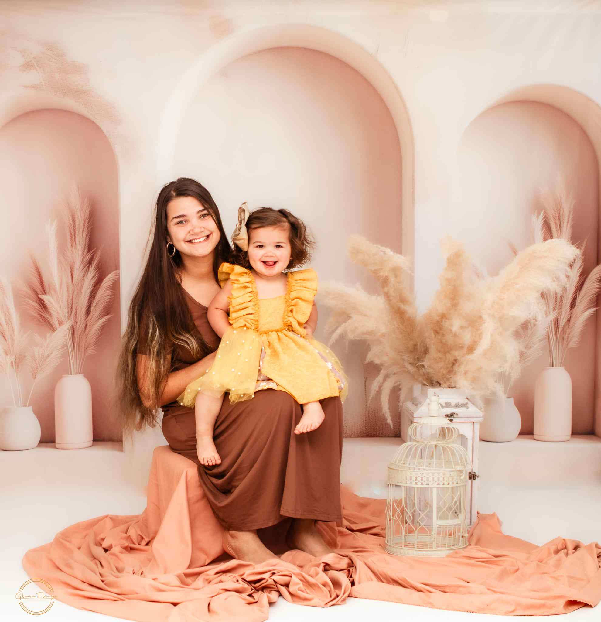 Mom holding daughter in front of beige arched wall Backdrop