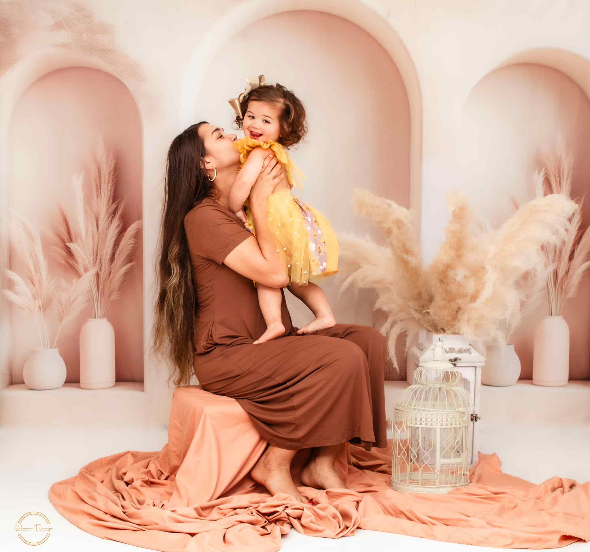 Mom holding daughter in front of beige arched wall Backdrop