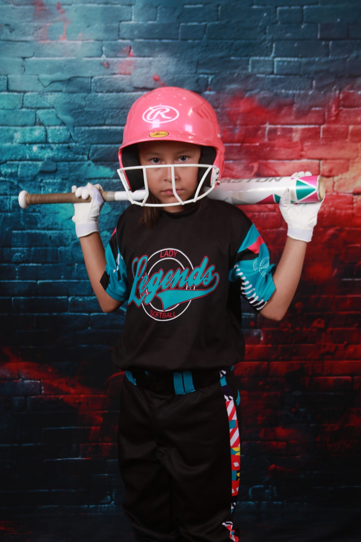 Girl holding a baseball bat standing in front of a turquoise brick wall backdrop