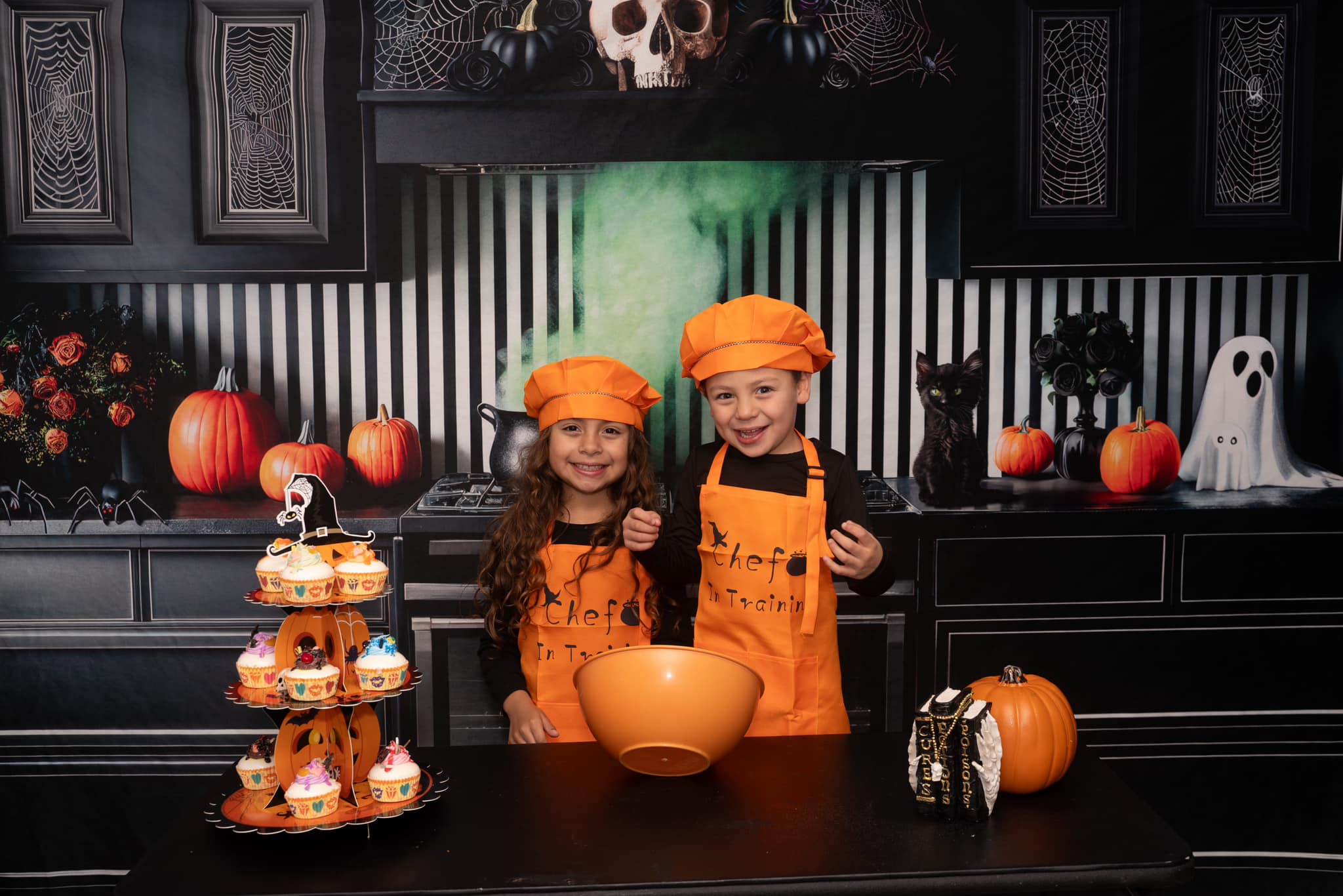 Two kids making pastries standing in front of Halloween kitchen backdrop