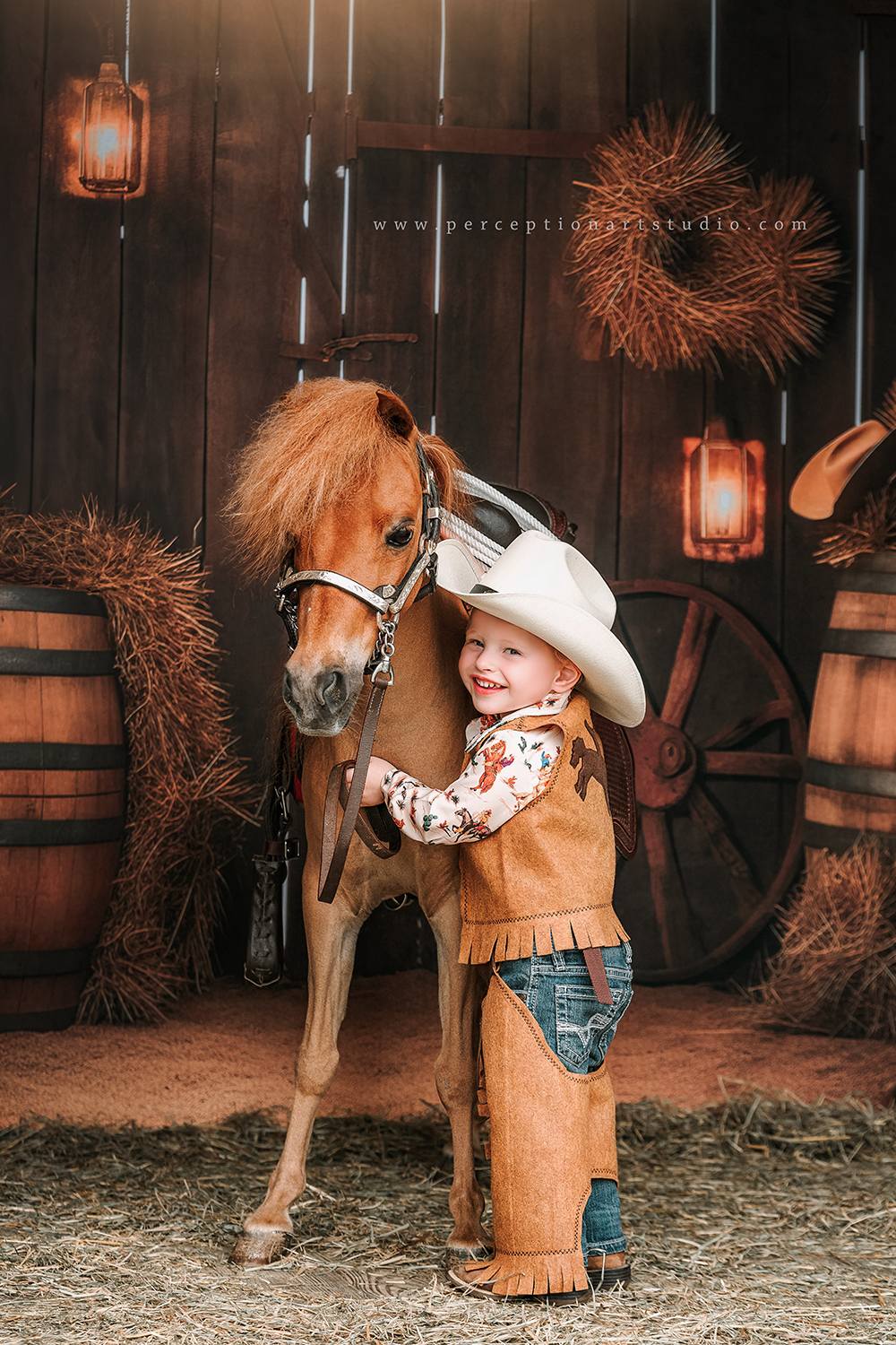 Little boy holding horse standing in front of autumn barn door backdrop