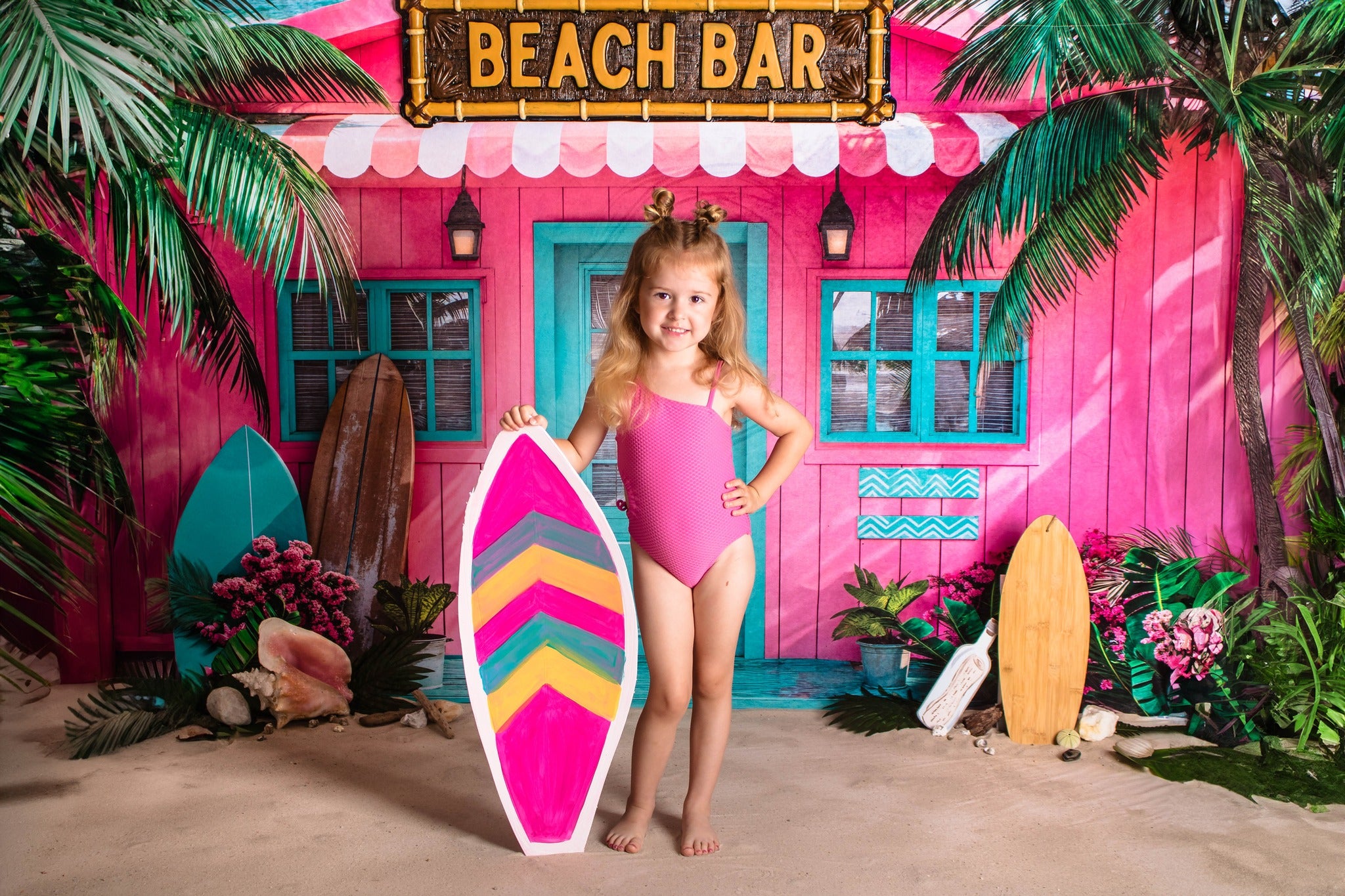 Girl holding surfboard standing in front of pink beach bar backdrop