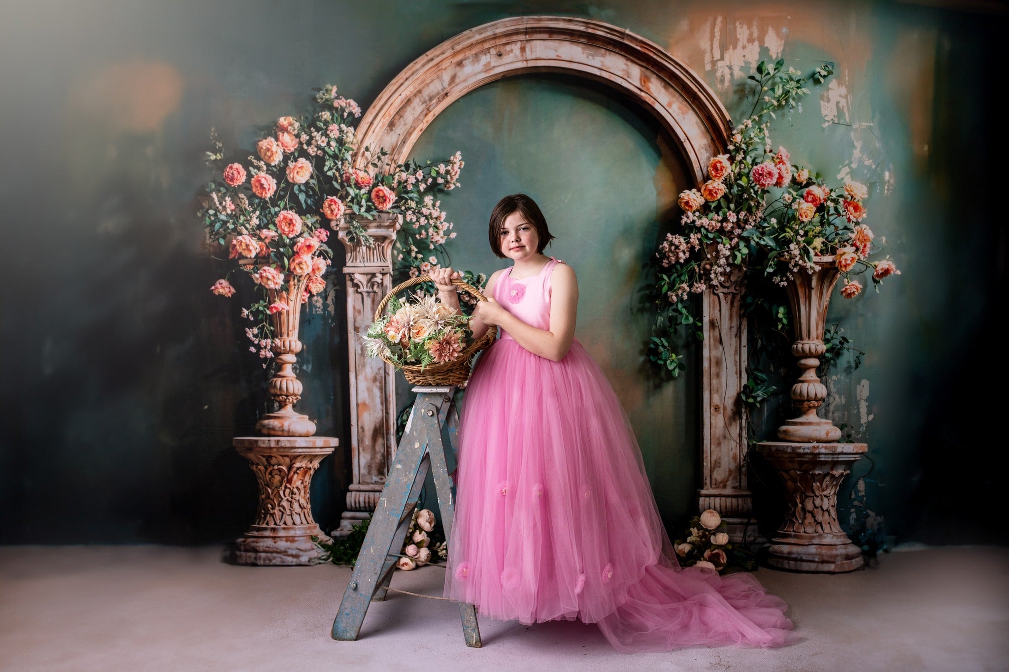 Girl in pink dress stands in front of spring arch backdrop