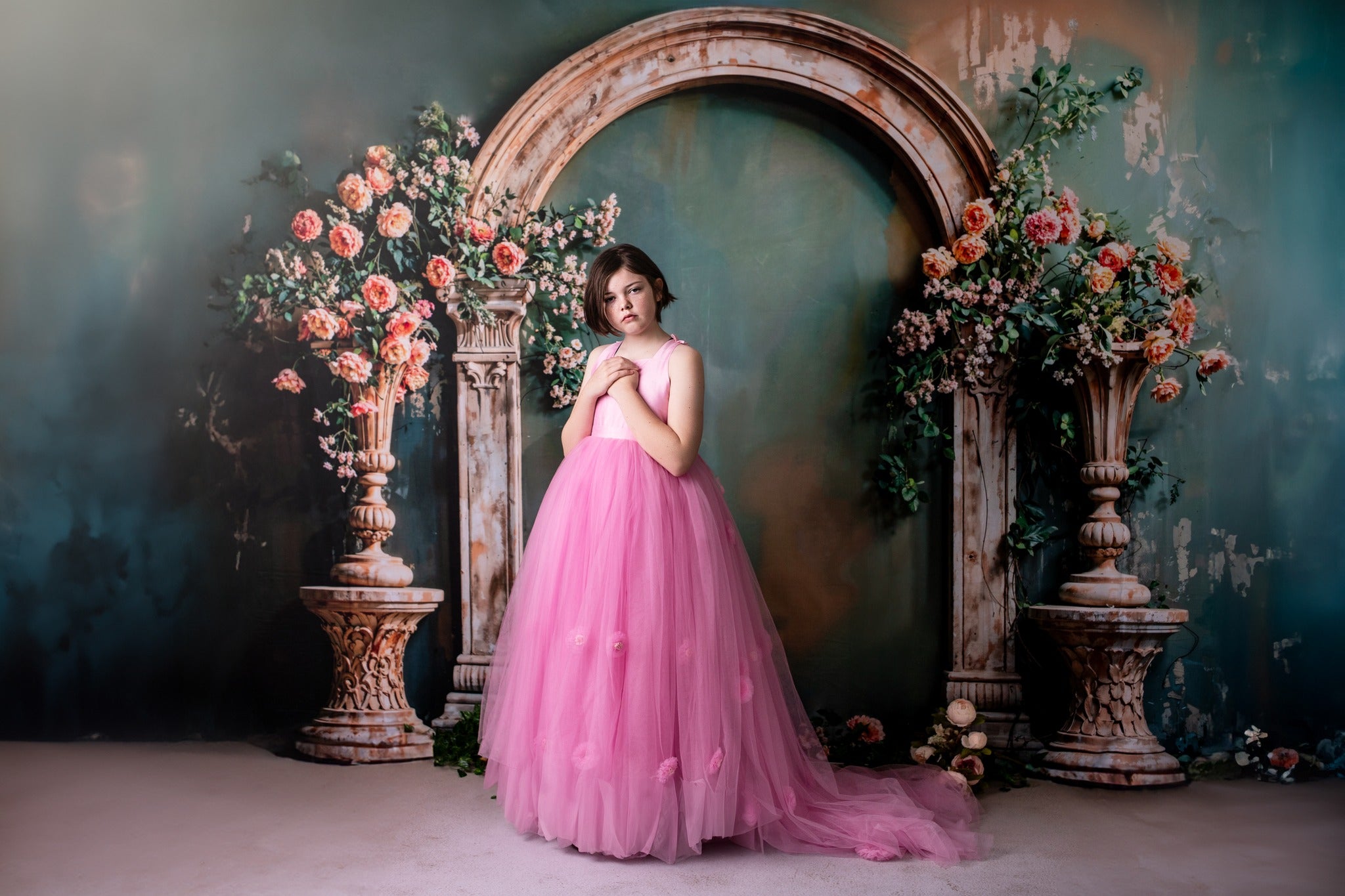 Girl in pink dress stands in front of spring arch backdrop