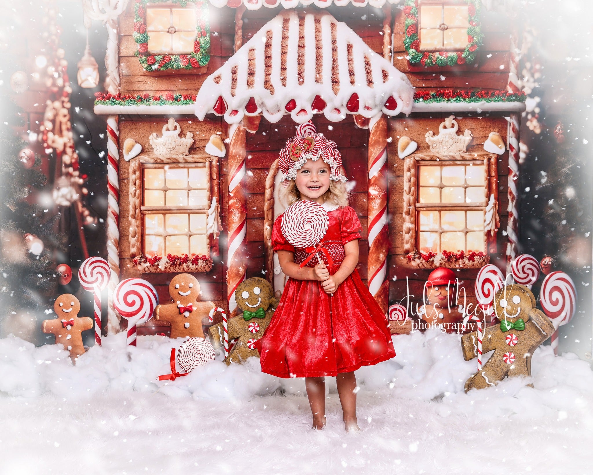 Girl in red dress standing in front of gingerbread house snowy backdrop