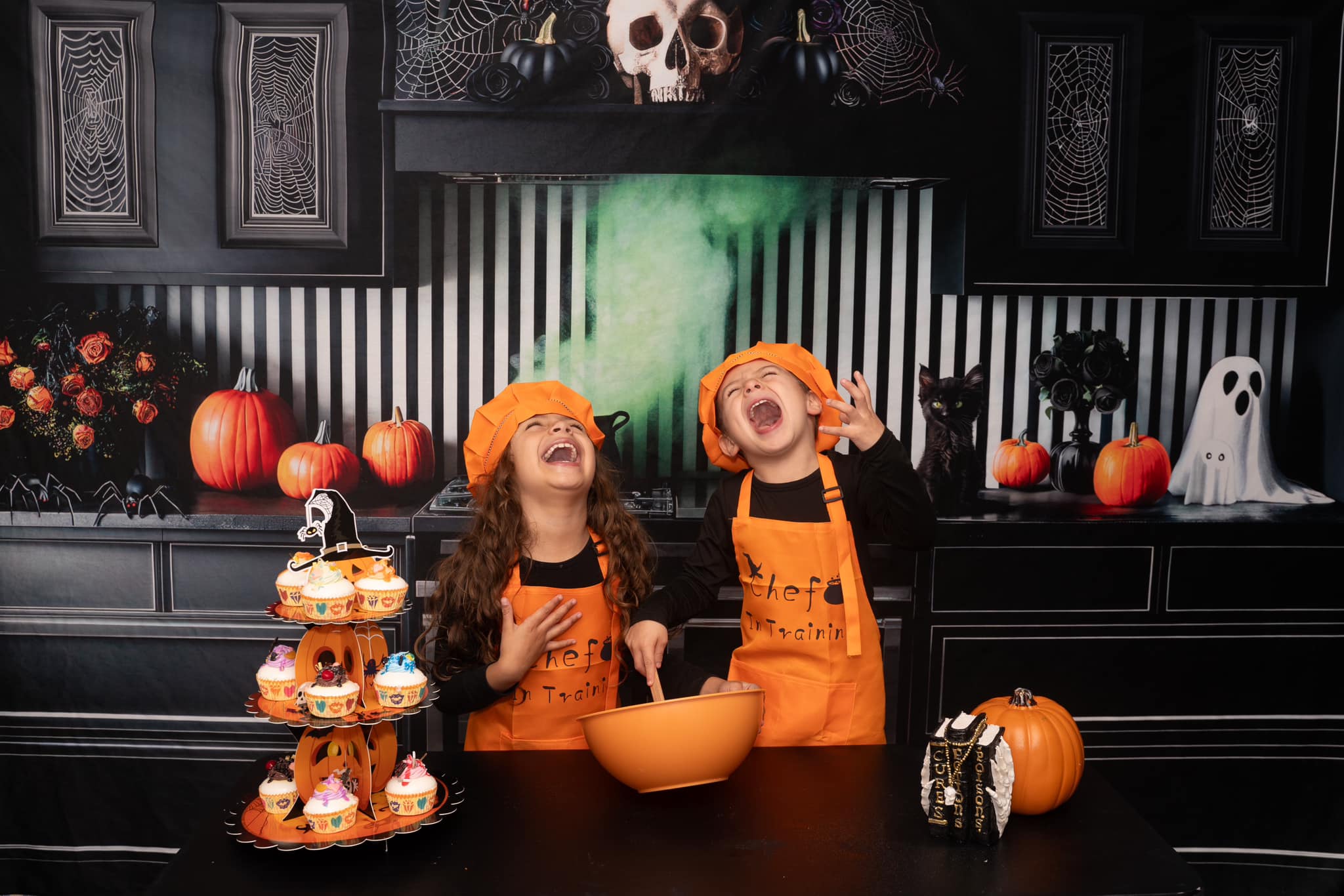 Two kids happily making pastries standing in front of Halloween kitchen backdrop