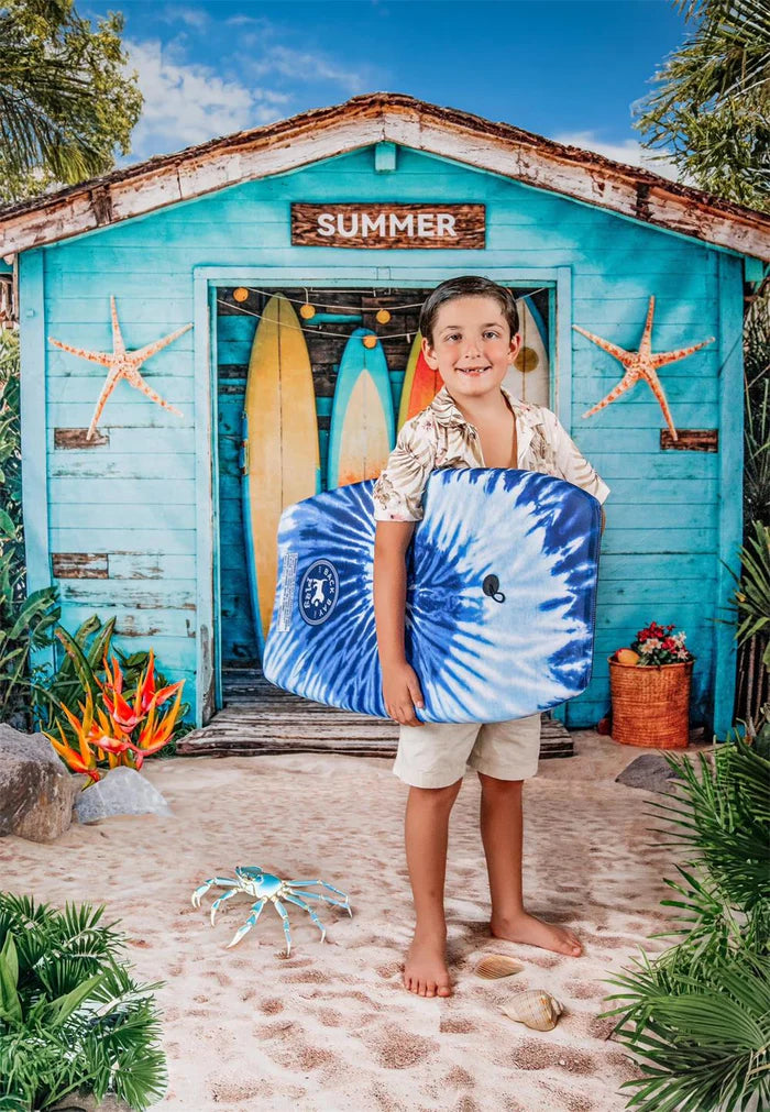 Boy holding surfboard sitting in front of summer fruit stand backdrop