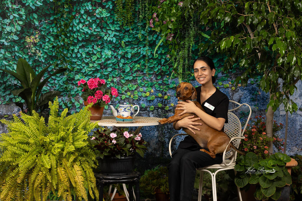 Girl holding dog sitting in front of green plant backdrop wall