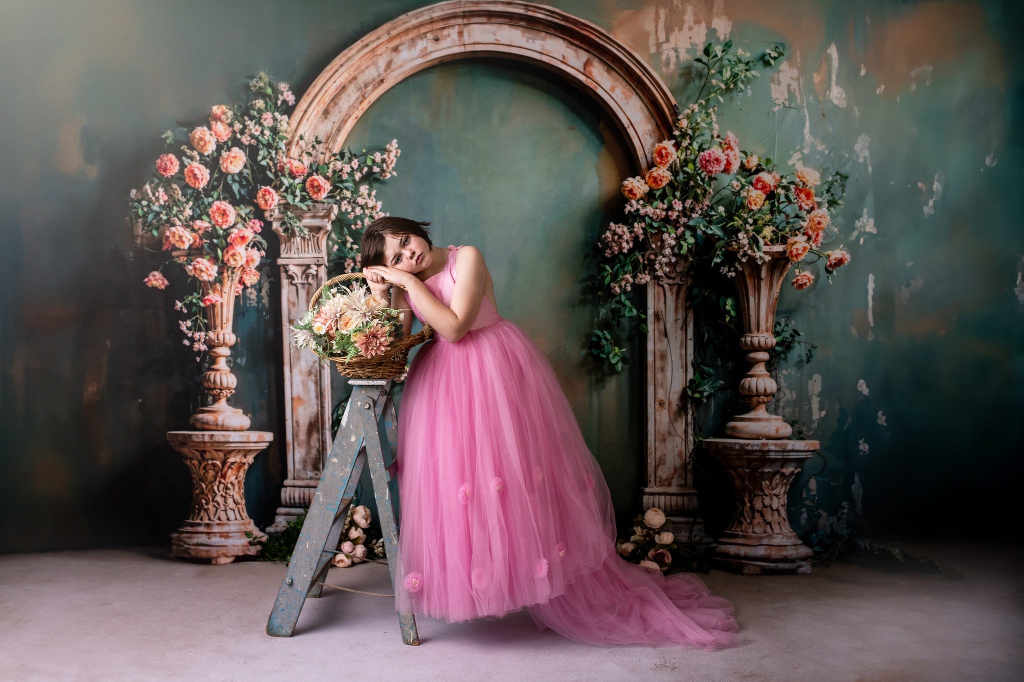 Girl in pink dress stands in front of spring arch backdrop