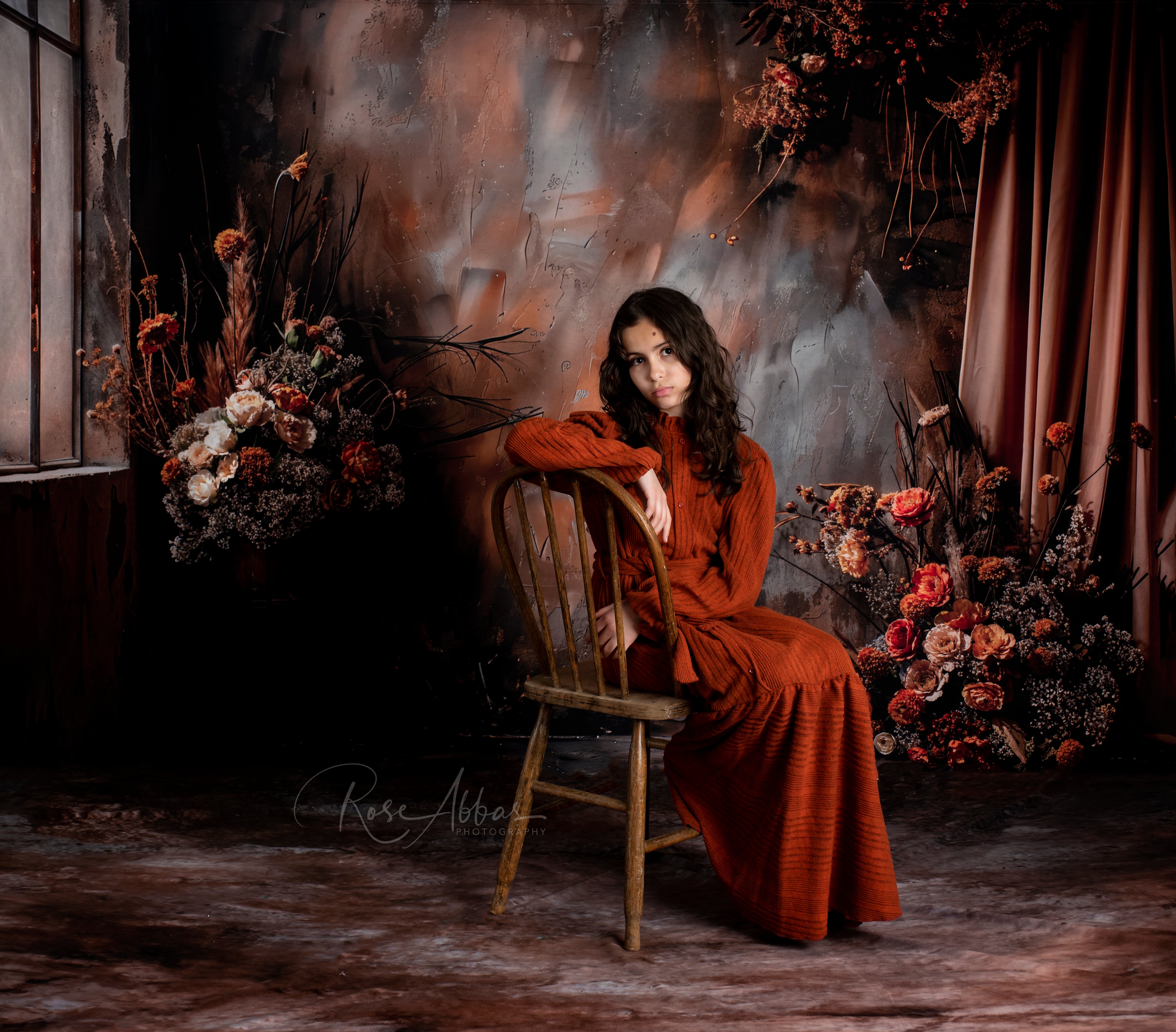 Girl in red dresss its on wooden chair in front of dark brown floral backdrop