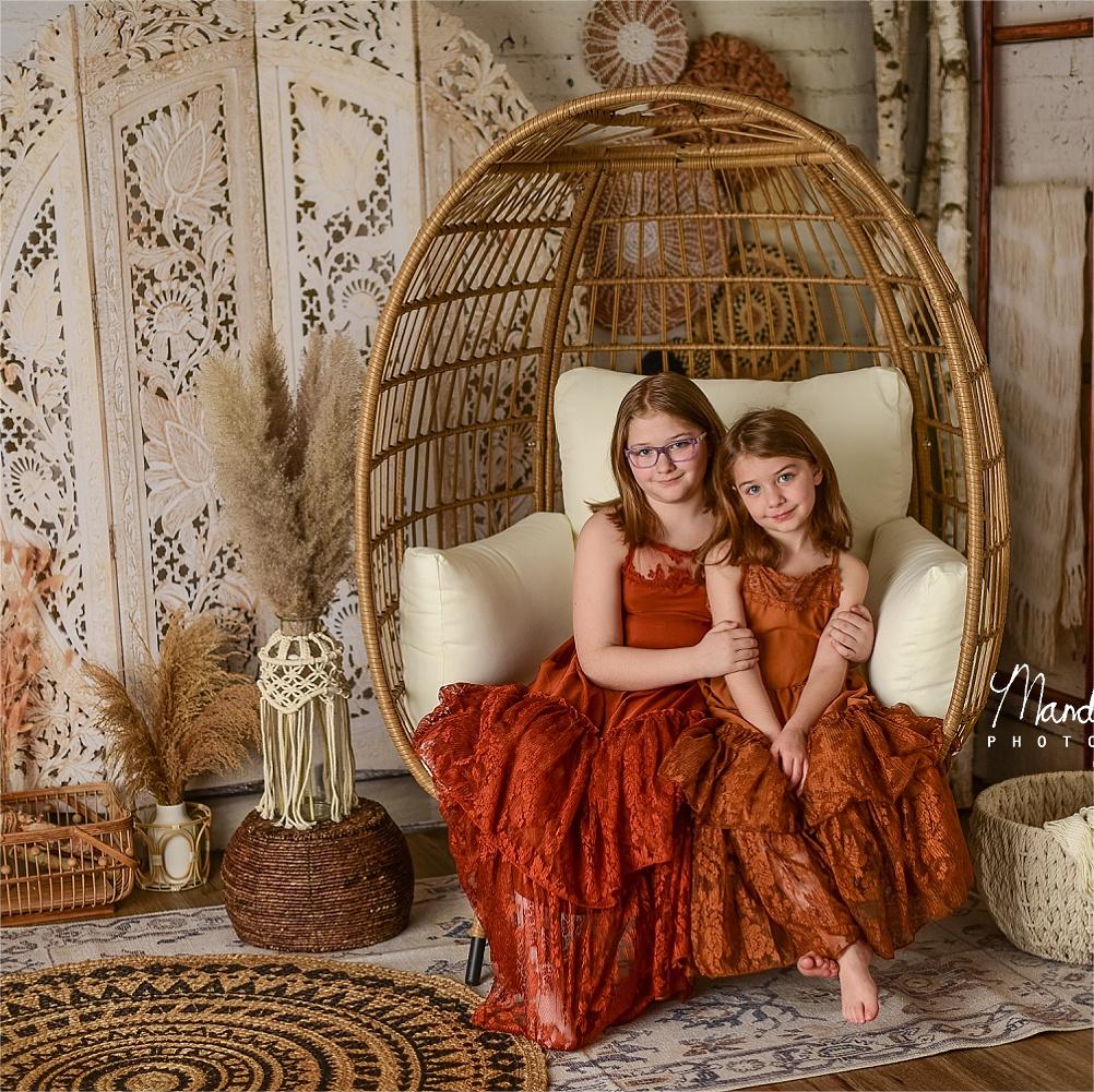 Sisters sitting in a cradle in front of a Boho screen backdrop