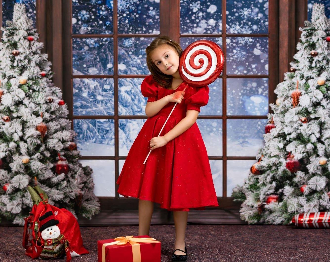 Girl holding candy standing in front of Christmas window backdrop