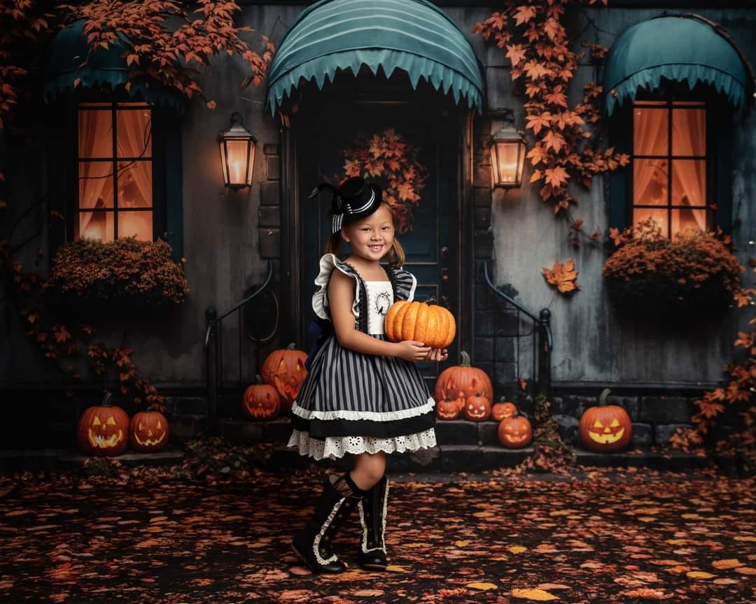 Little girl holding a pumpkin standing in front of Halloween fallen leaves backdrop