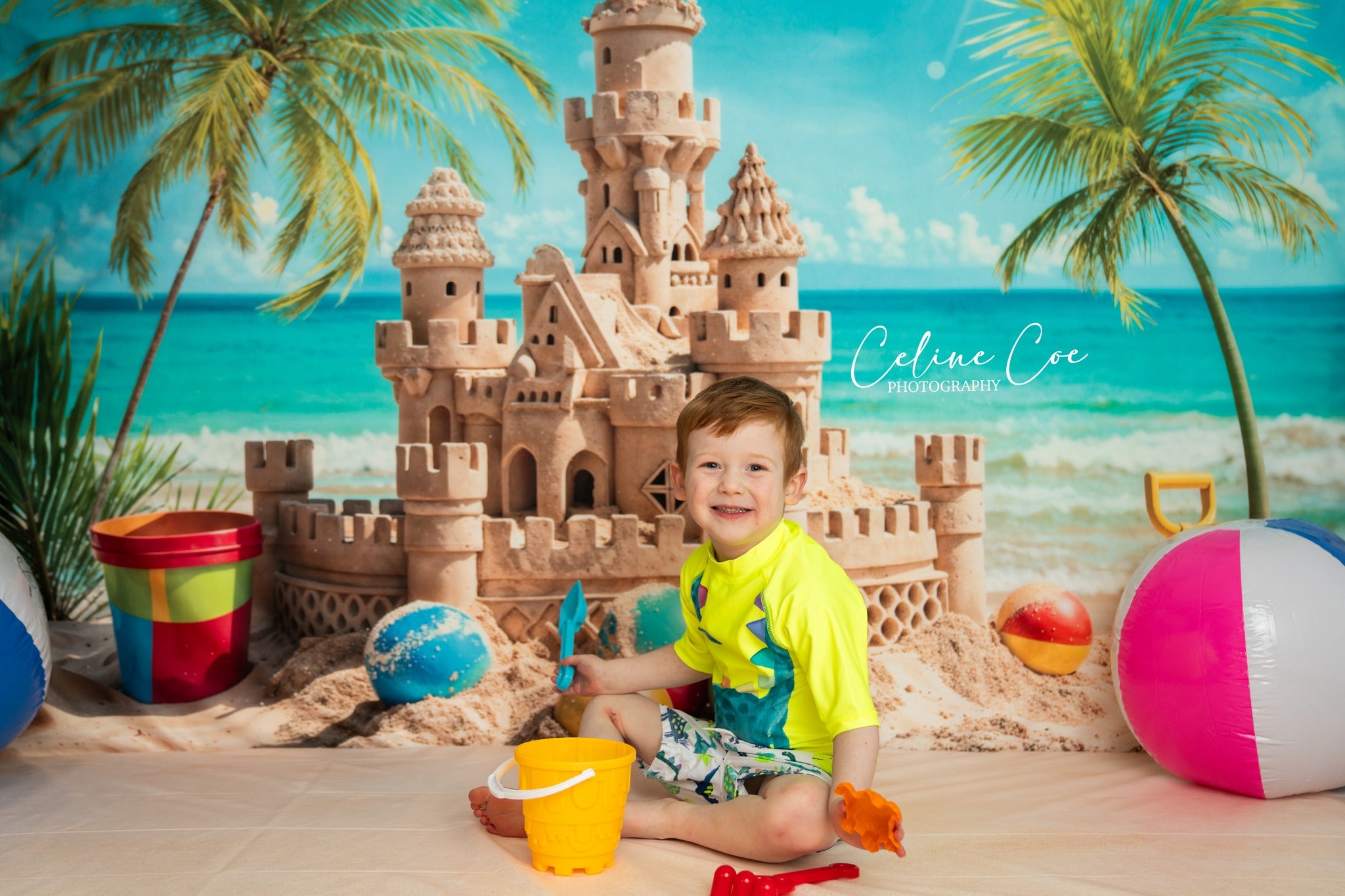 Boy playing with sand sitting in front of sand castle backdrop