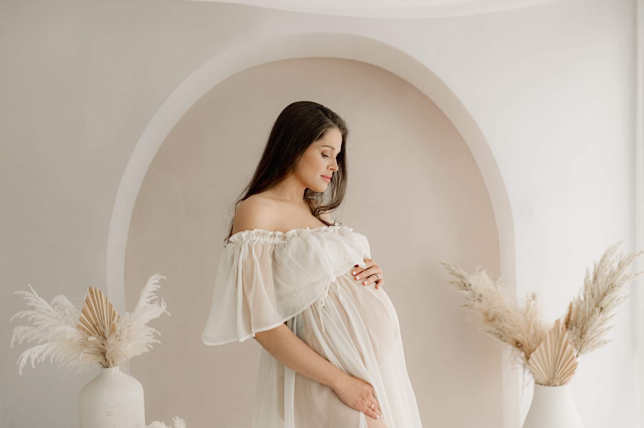 Pregnant woman standing in front of boho arch  backdrop