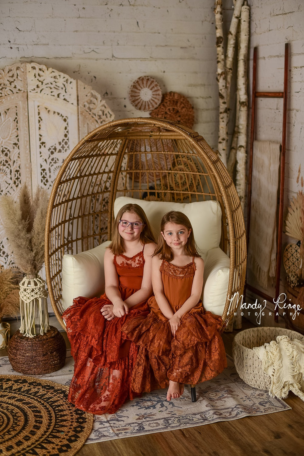 Sisters in red dresses sit in cradle in front of Boho Macrame Wall Backdrop